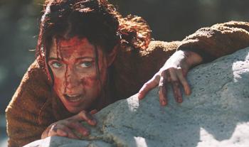 A woman with a bloodied face clings to a rock cliff.