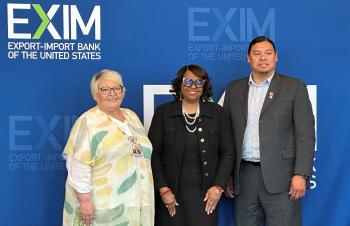 Two woman and one man stand in front of a blue background with the words EXIM printed in the left-hand top corner.