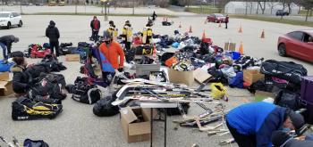 Hockey equipment is scattered across a parking lot as people go through and choose what they need for their children's hockey bags.