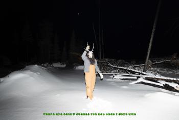 A man walks at night throug the snow. He holds a caribou skull in front of his face.