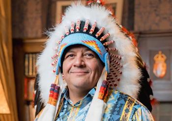 A man in a chief's feather headdress smiles at the camera.