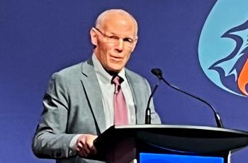 A man stands at a lecturn and speaks into a microphone.