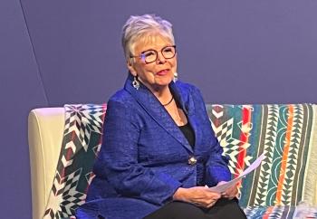 A woman sits on a couch as she speaks.