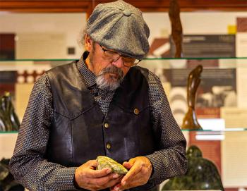 A man wearing a flat cap looks down at a rock in his hands.
