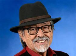 A man wearing a fedora smies at the camera.