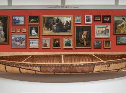 A birchbark canoe is dispayed before a wall of painting.