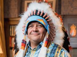 A man in a chief's feather headdress smiles at the camera.