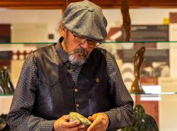A man wearing a flat cap looks down at a rock in his hands.